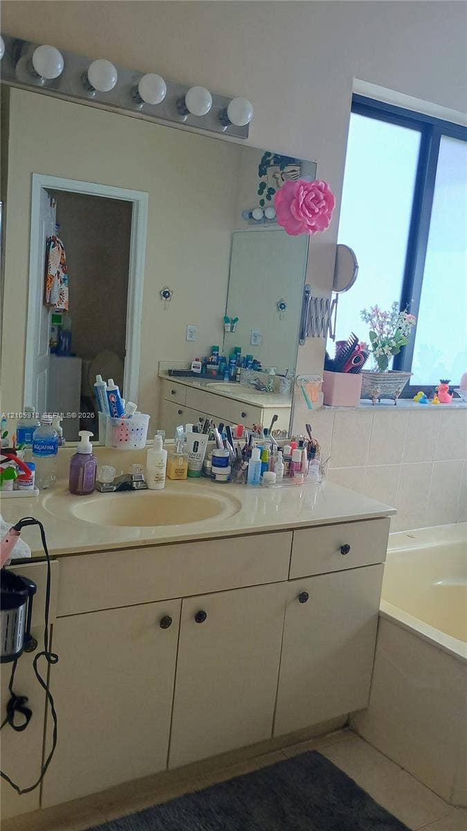 3253 SW 150 Court, Miami, FL 33185 Bathroom vanity featuring a solid-surface countertop with an integrated basin, multi-door cabinetry with dark hardware, a large wall-to-wall mirror, and a five-bulb vanity light fixture