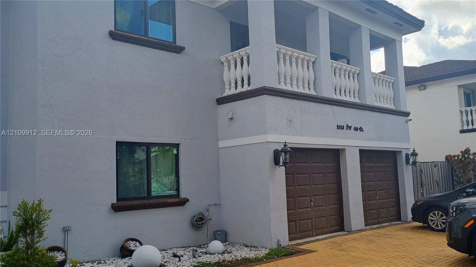 3253 SW 150 Court, Miami, FL 33185 Two-story exterior featuring a stucco facade, covered upper-level balcony with white balustrade railings, two-car garage with paneled doors, and paved driveway