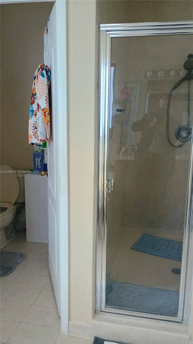 3253 SW 150 Court, Miami, FL 33185 Glass-enclosed shower with chrome frame and adjustable handheld showerhead, accompanied by tile flooring and a standard porcelain toilet