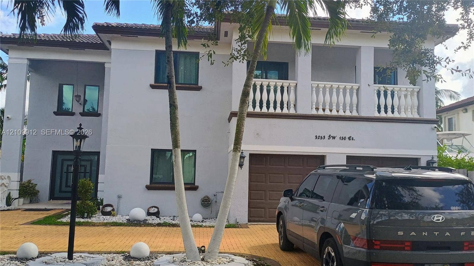3253 SW 150 Court, Miami, FL 33185 Two-story residence featuring a paved driveway, a second-floor balcony with balustrade railing, a tiled roof, and a two-car garage