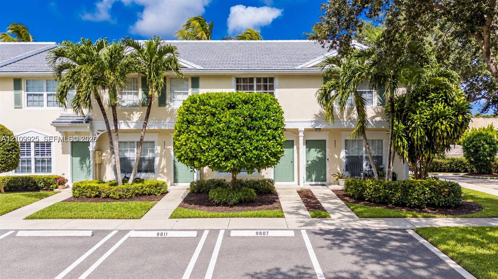 9807 NW 57th Manor, Coral Springs, Coral Springs, FL 33076 Two-story townhome exterior featuring light-toned stucco siding, a grey shingle roof, multi-pane windows, and designated asphalt parking