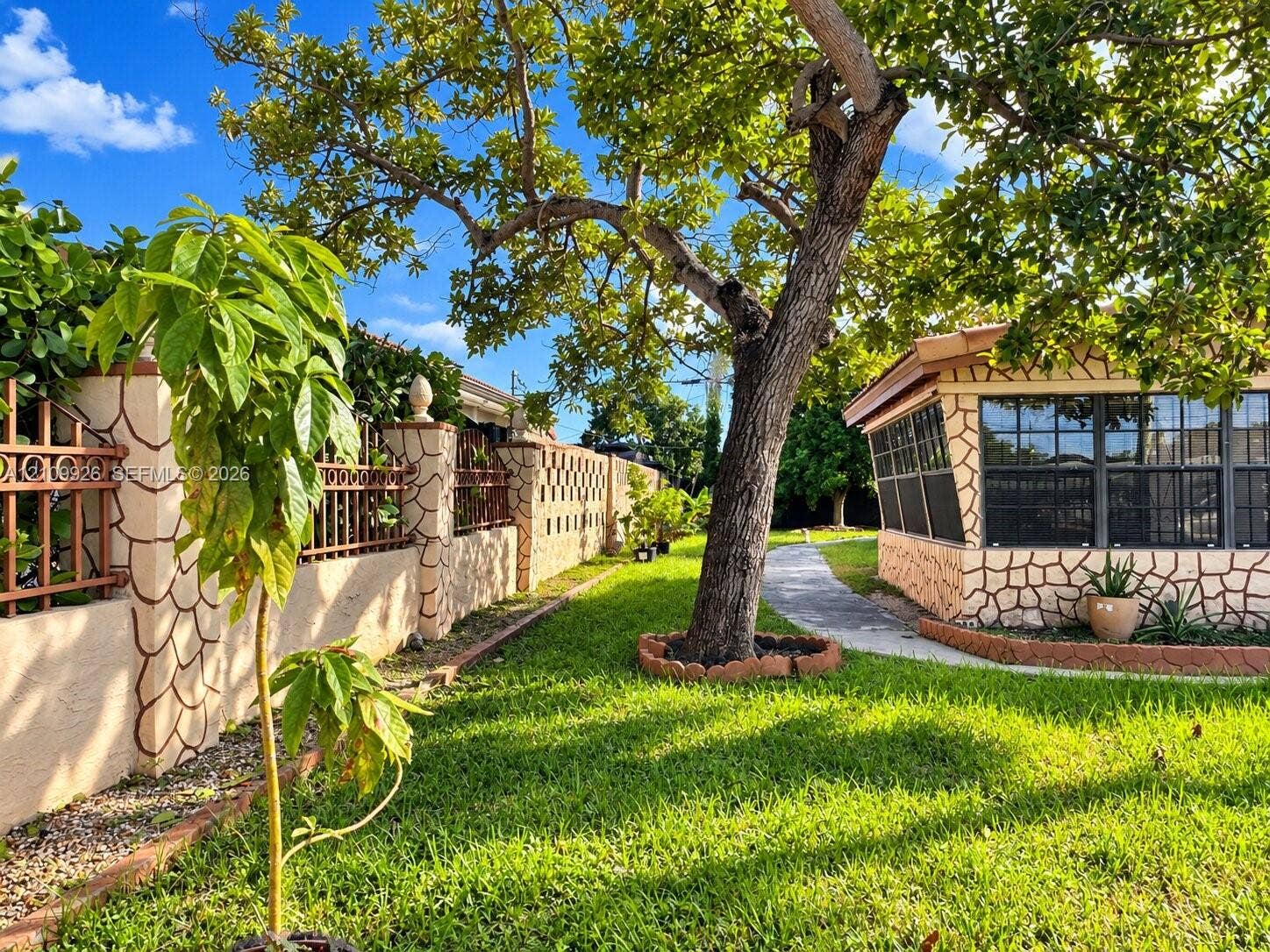 1440 NW 183rd Street, #0, Miami Gardens, Miami Gardens, FL 33169 Exterior area featuring stone-clad masonry walls, a screened-in structure with grid windows, mature landscaping, and a concrete pathway