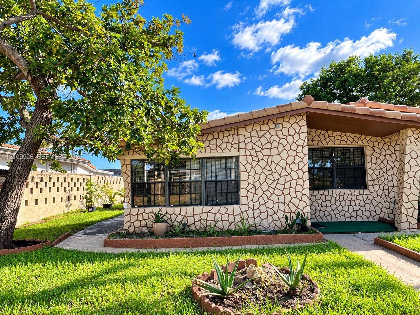 1440 NW 183rd Street, #0, Miami Gardens, Miami Gardens, FL 33169 Exterior featuring decorative stone-patterned facade, mission-style tile roof, multi-pane windows, and a landscaped front yard with concrete border edging
