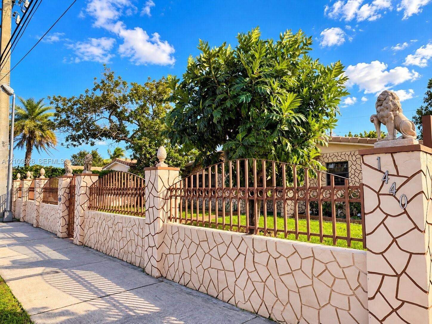 1440 NW 183rd Street, #0, Miami Gardens, Miami Gardens, FL 33169 Custom masonry boundary wall featuring decorative stone cladding, ornamental metal fencing, and integrated stone lion statuary