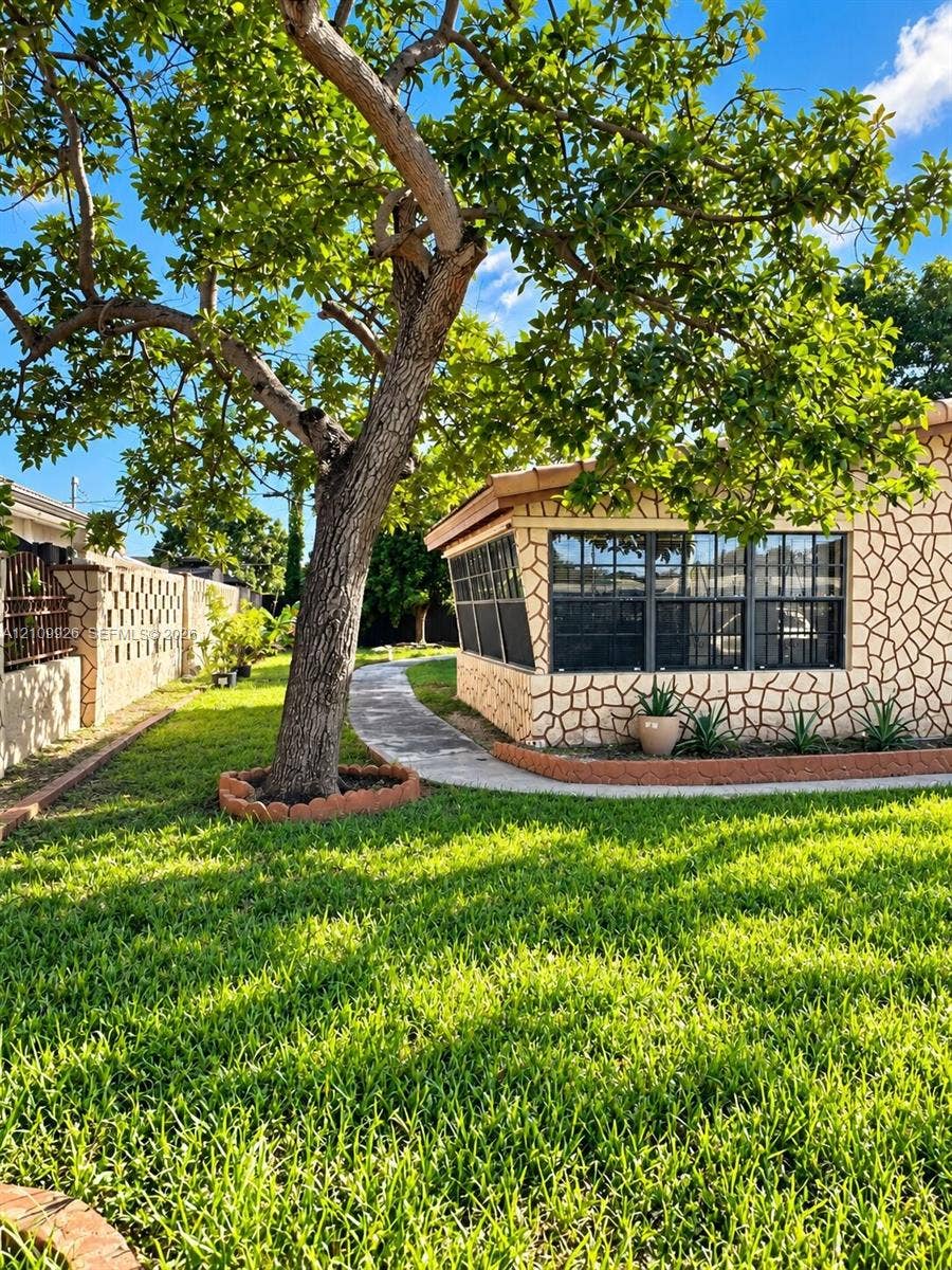1440 NW 183rd Street, #0, Miami Gardens, Miami Gardens, FL 33169 Spacious backyard featuring a manicured lawn, stone-patterned exterior masonry, mature canopy tree, concrete pathway, and concrete block perimeter wall