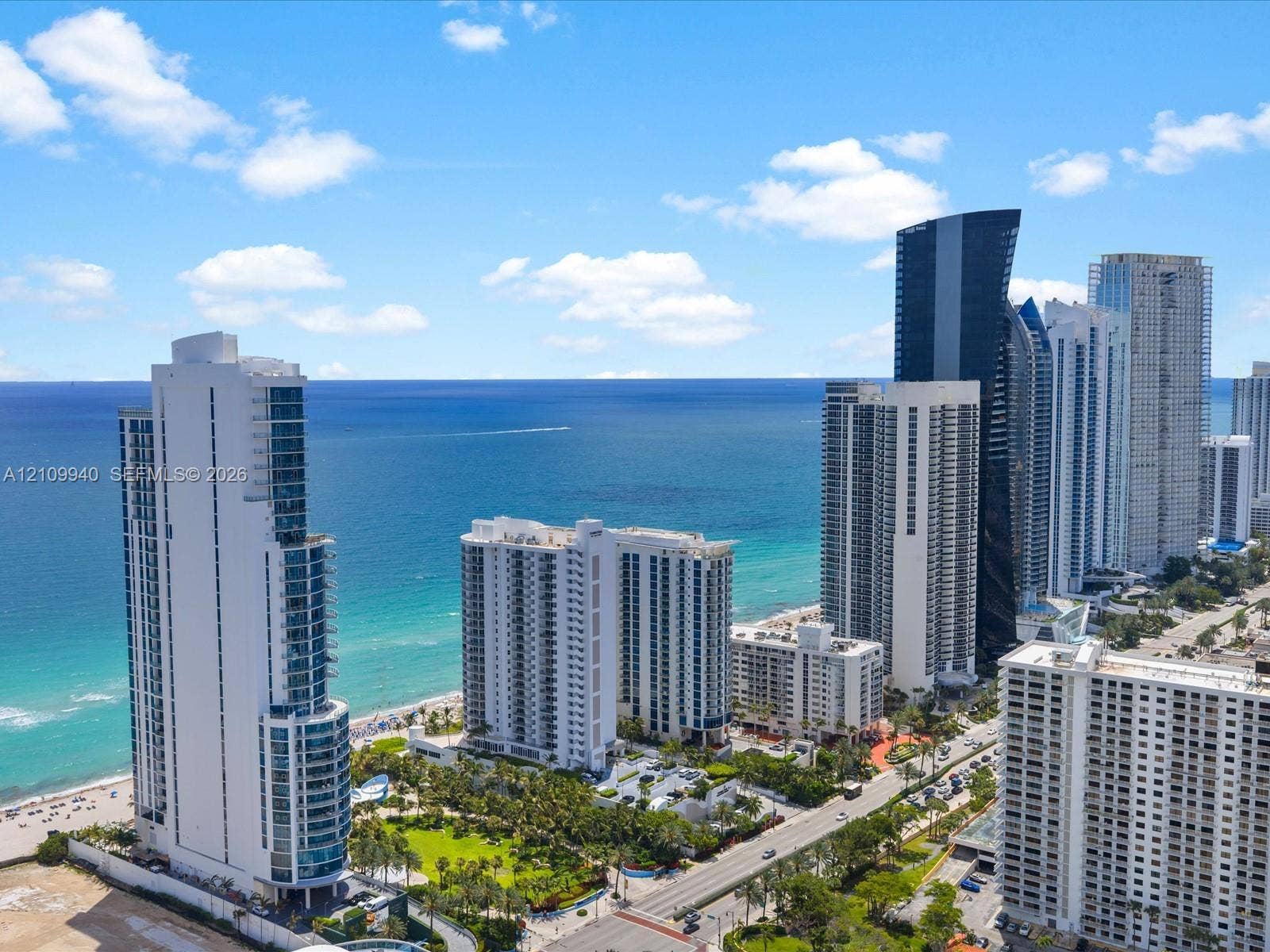 Aerial perspective of coastal high-rise development featuring expansive ocean frontage, pristine sandy shoreline, and mature tropical landscaping