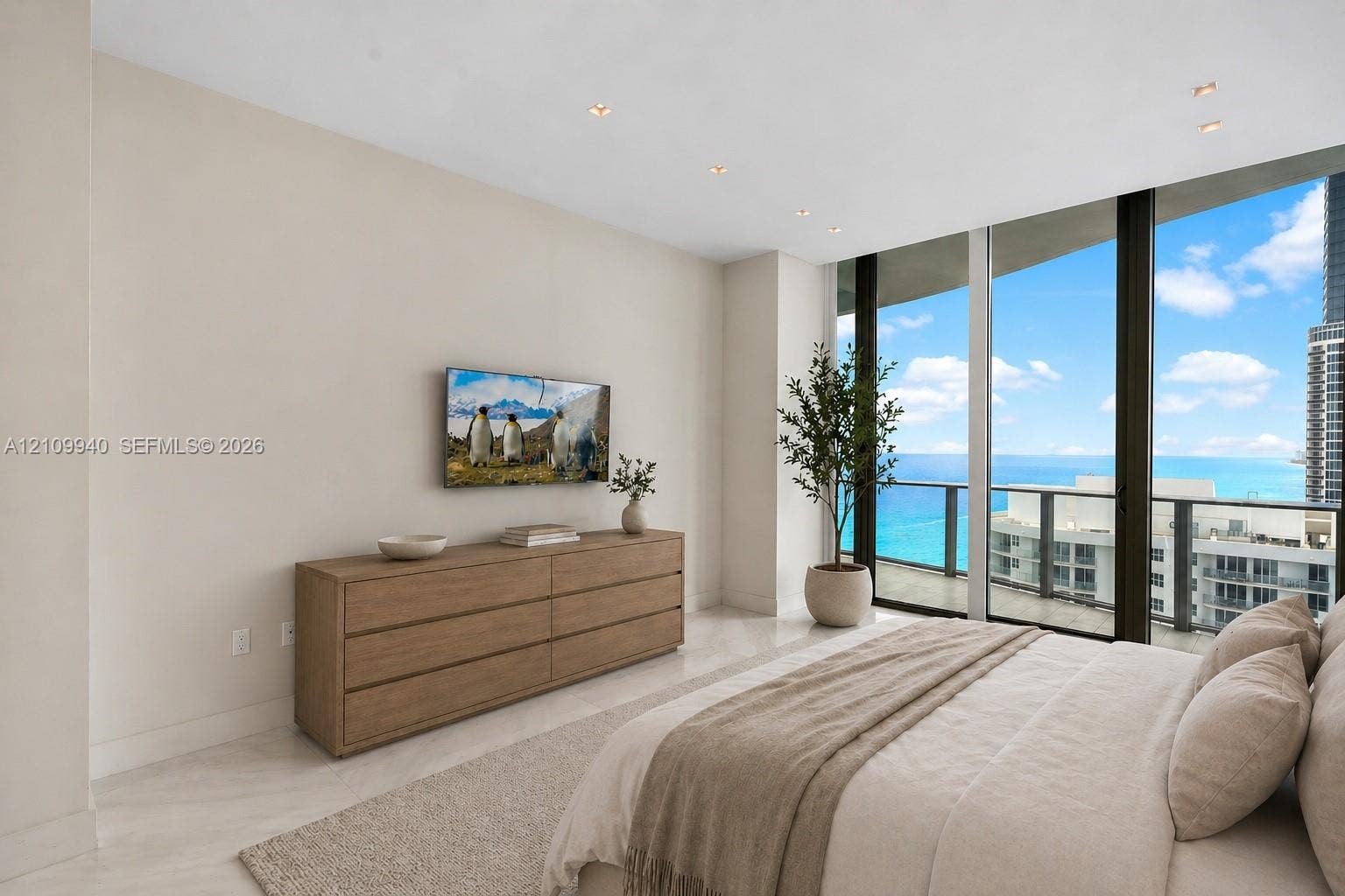 Floor-to-ceiling windows, light-toned stone-finish flooring, recessed lighting, and a private balcony with water scenery