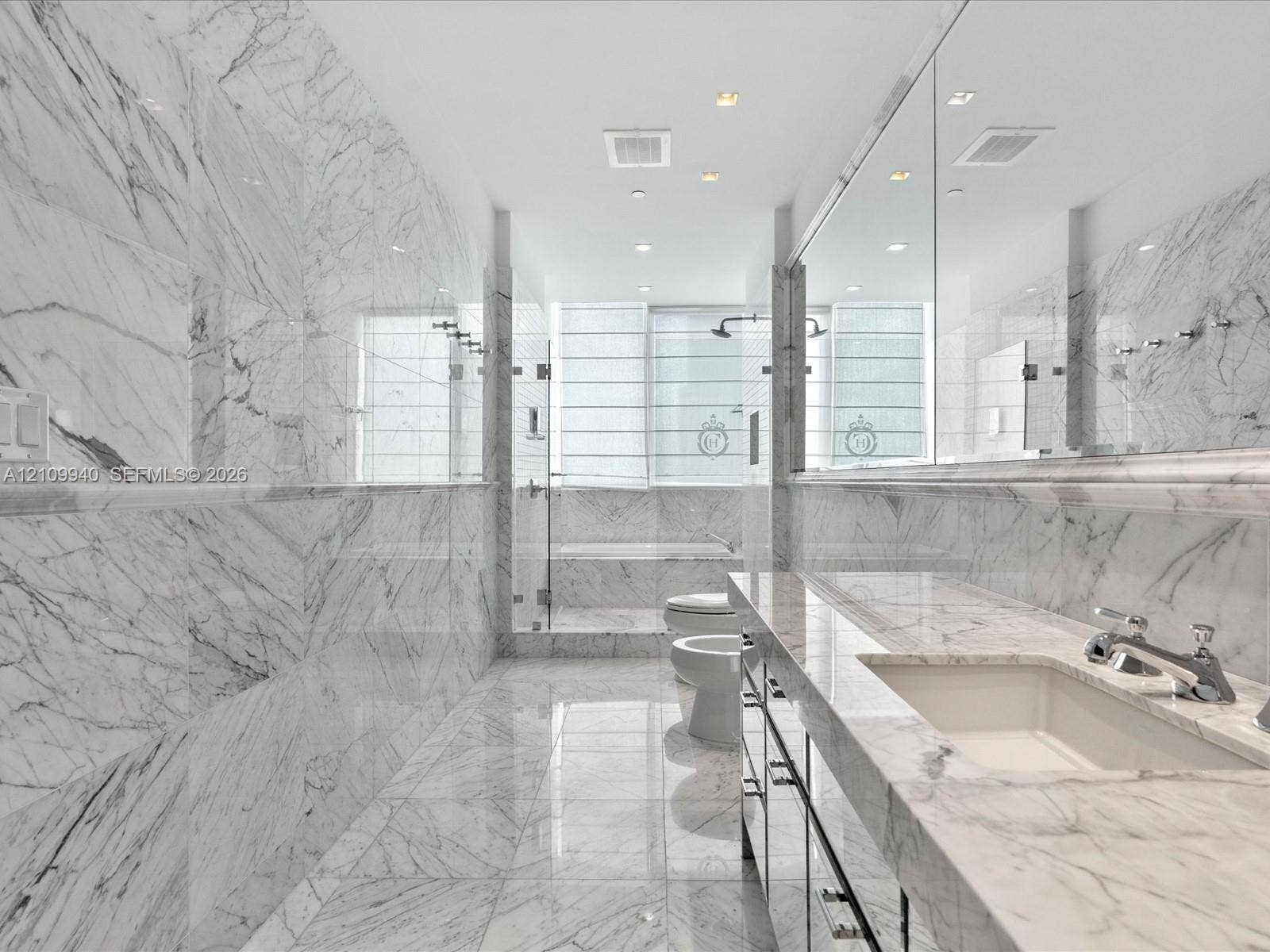 Full-height stone wall tiling, expansive vanity with a stone countertop, integrated undermount sink, recessed ceiling lighting, and a glass-enclosed shower area
