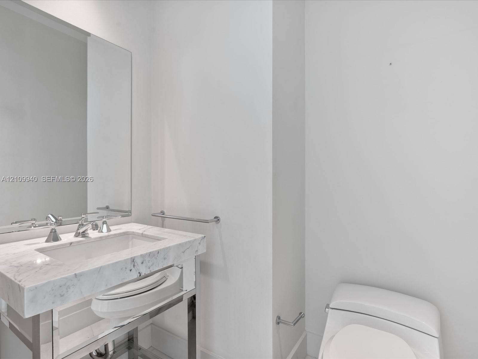Stone-topped console vanity with integrated rectangular sink, chrome metal-finish base, wall-mounted mirror, and polished chrome hardware