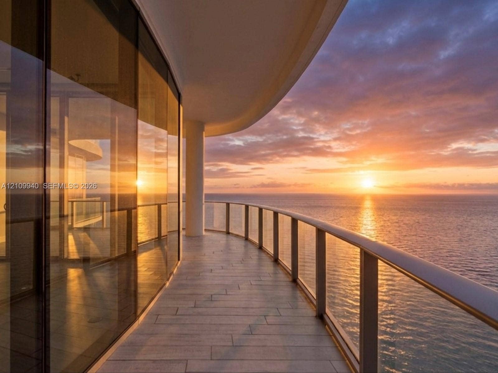 Curved balcony featuring tile flooring, full-height glass walls, and a glass-panel railing, set against a coastal backdrop