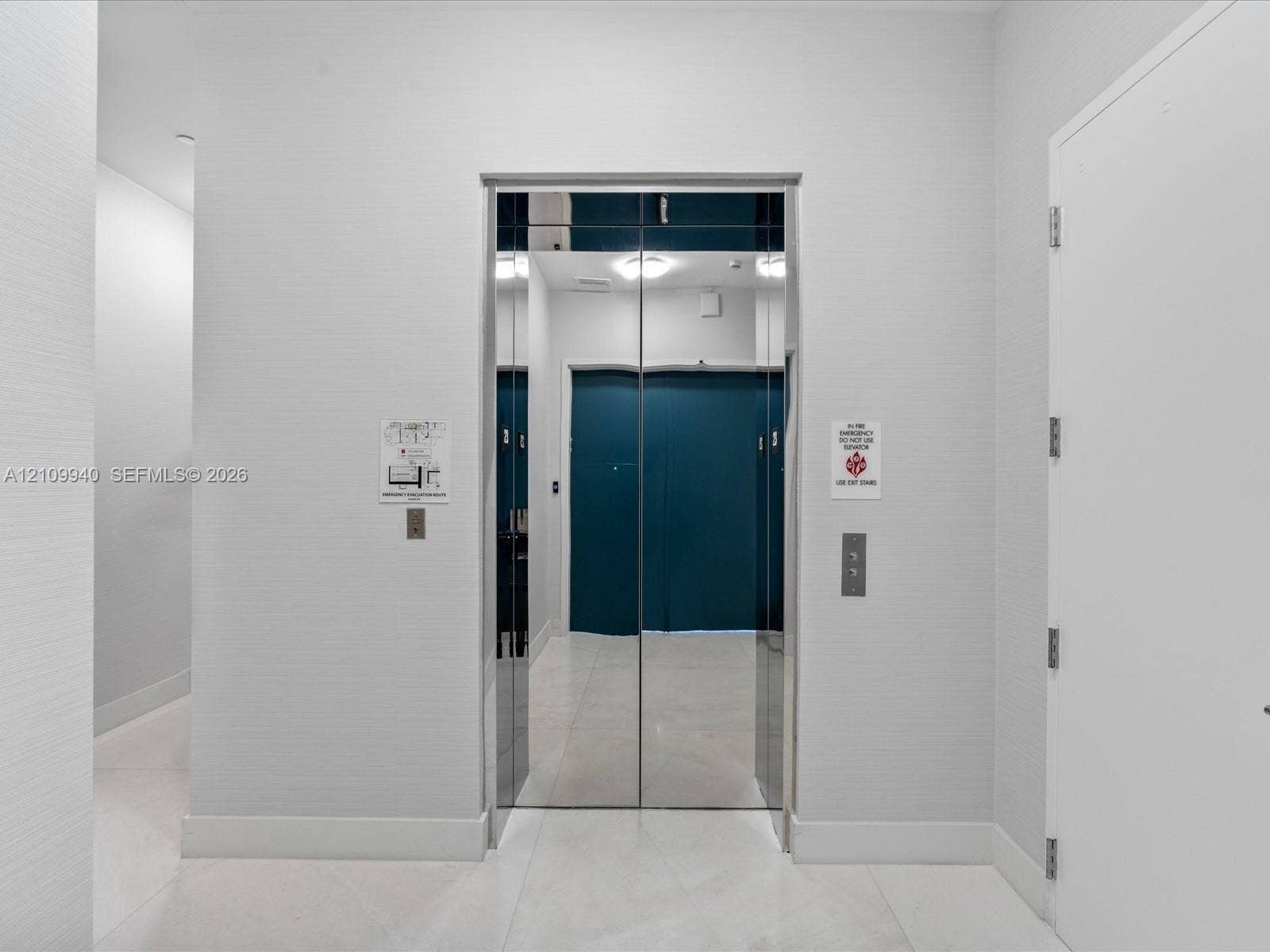 Elevator entrance featuring mirrored doors, metallic call buttons, and large-format tile flooring