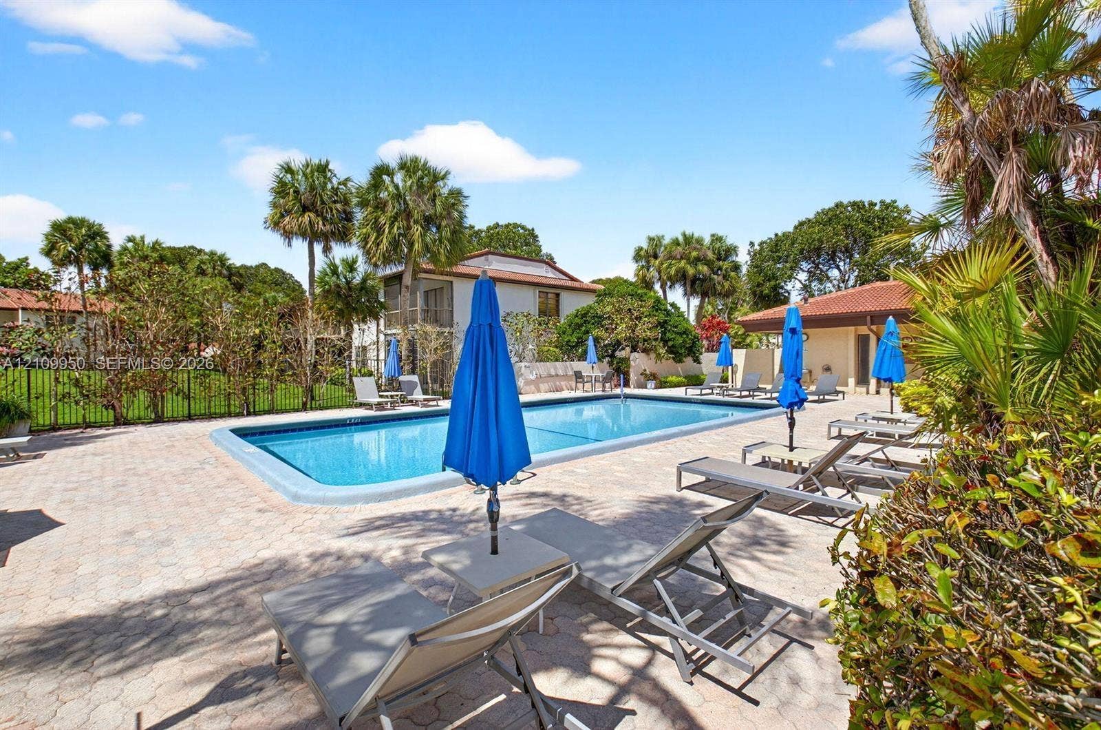 In-ground swimming pool with stone-paver decking, perimeter metal fencing, and mature palm trees