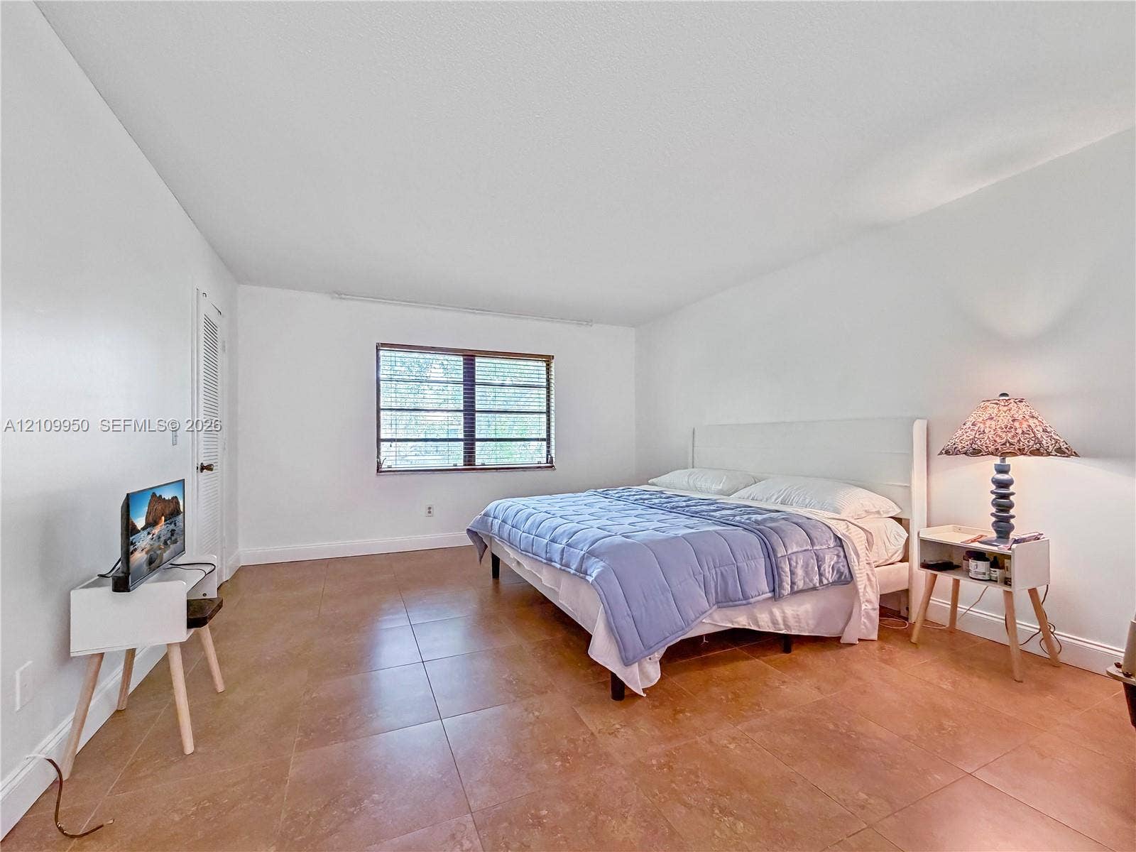 Spacious room featuring neutral wall tones, large-format tile flooring, and a multi-pane window with dark-finish trim