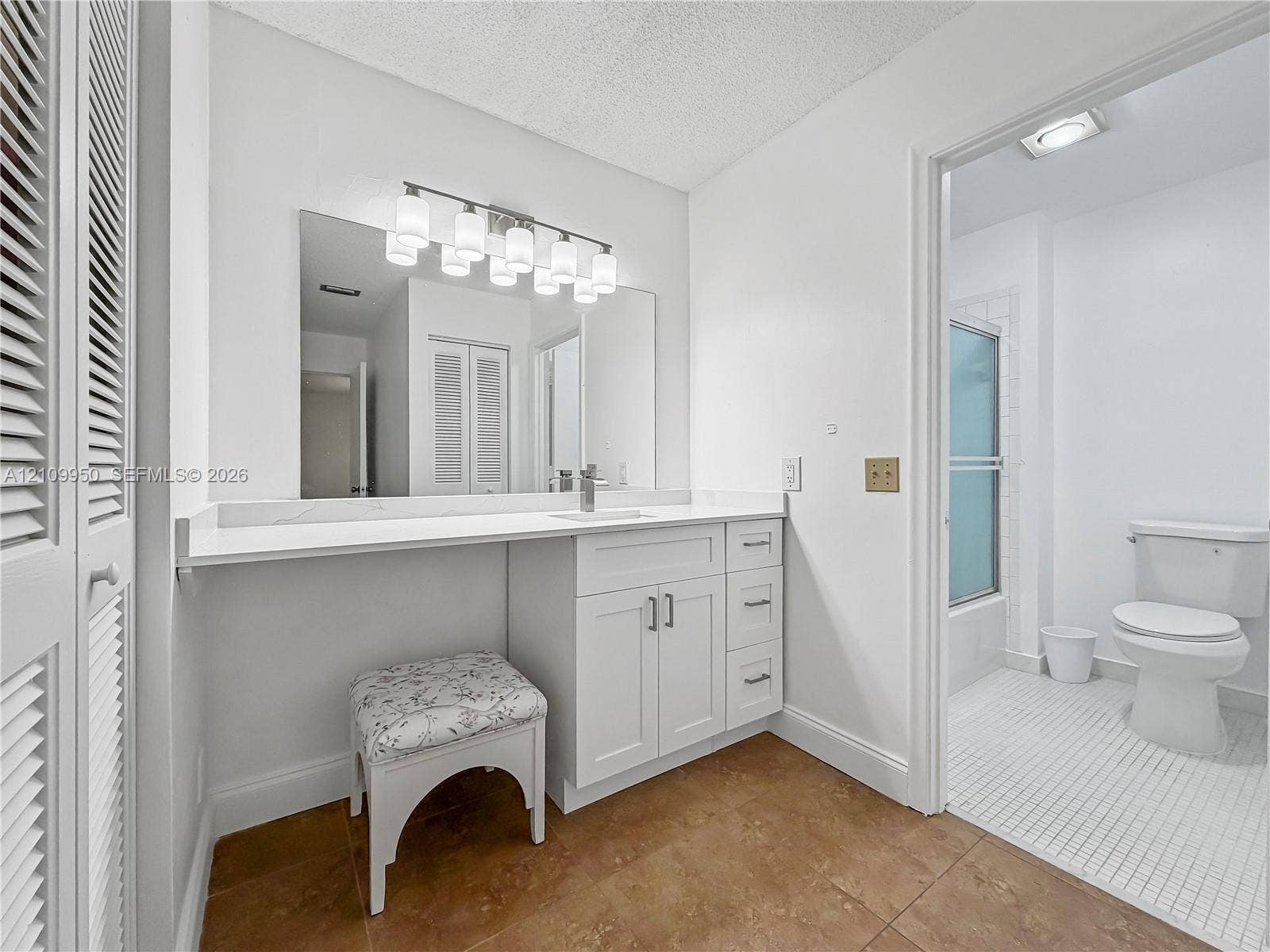 Bathroom featuring a white vanity with extended countertop, large wall-mounted mirror, multi-bulb lighting fixture, and a tile floor