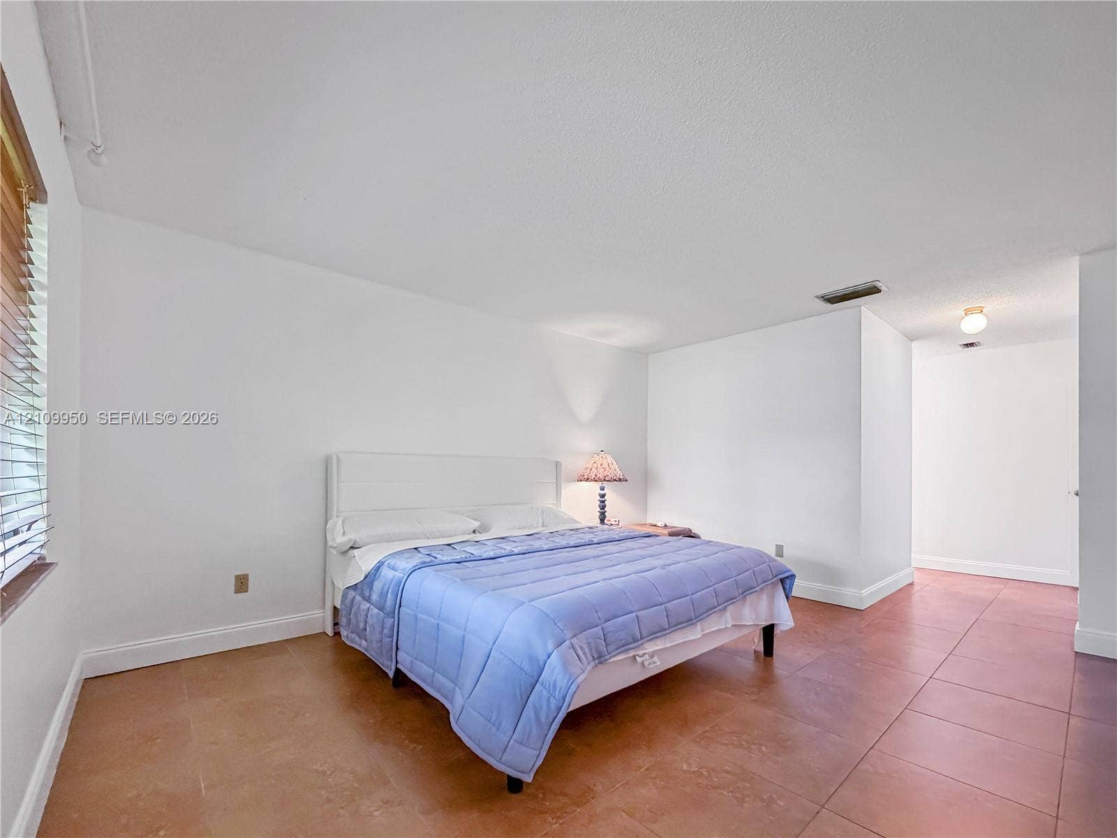 Spacious interior room featuring terracotta-style tile flooring, neutral wall finishes, and horizontal window blinds