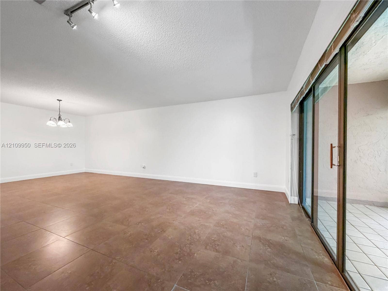 Open-concept interior featuring large-format stone-finish tile flooring, ceiling-mounted track lighting, a multi-arm chandelier, and sliding glass doors