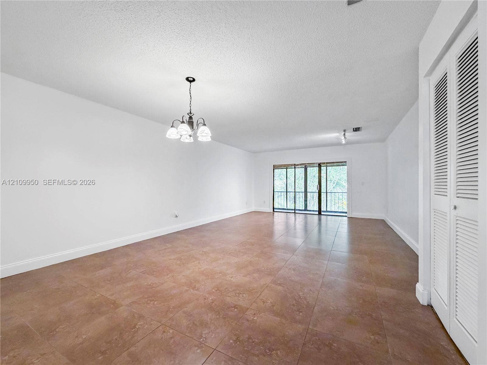 Large room featuring oversized tile flooring, a multi-light chandelier, sliding glass doors, and louvered double-door closets