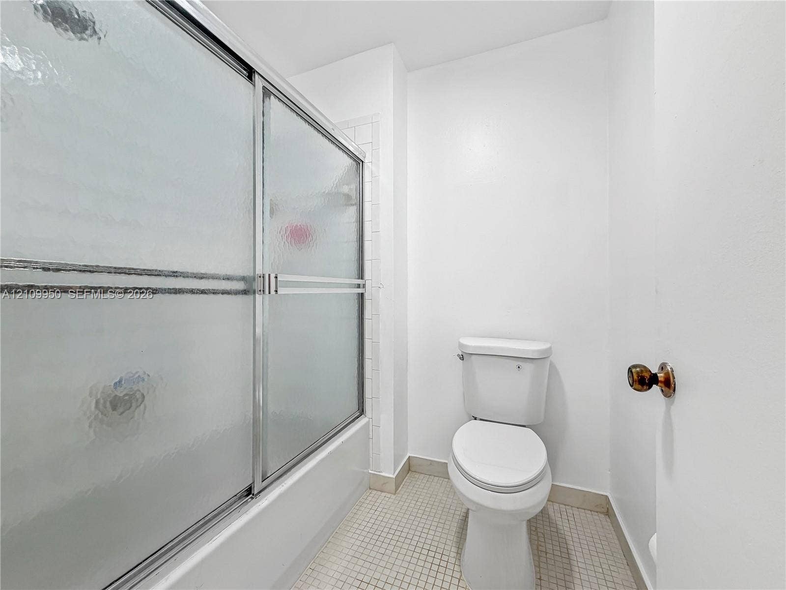 Bathroom featuring a shower with a sliding metal-framed textured glass enclosure, white tile shower surround, and square floor tiling