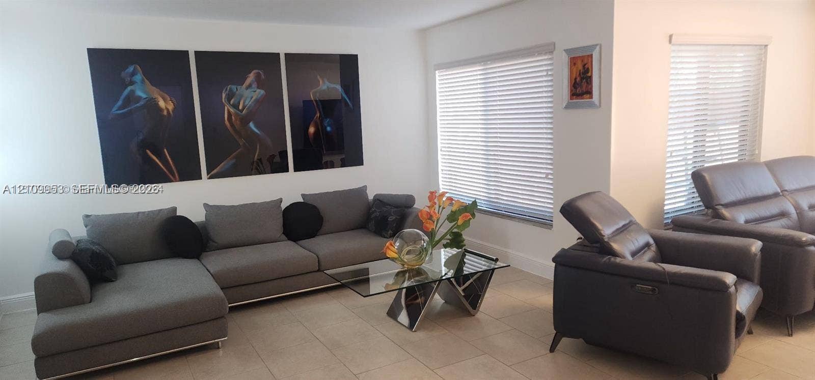 Neutral-toned interior space featuring light-colored tile flooring and multiple windows with horizontal blinds