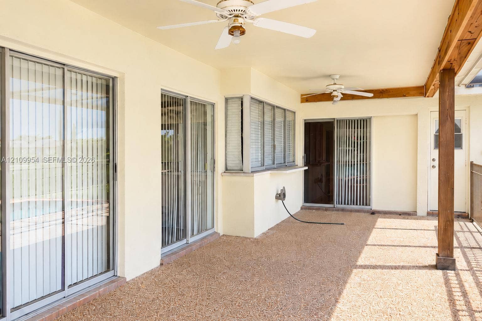 8528 Windsor Drive, Miramar, FL 33025 Covered patio featuring aggregate concrete flooring, dual ceiling fans, multiple sliding glass door entries, and exposed timber support beams