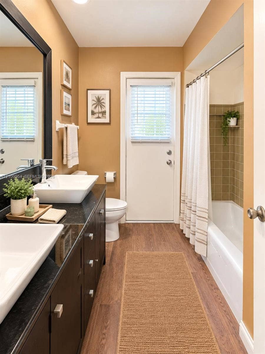 8528 Windsor Drive, Miramar, FL 33025 Dark-finish vanity with dual rectangular vessel sinks, contrasting solid-surface countertop, wood-finish flooring, and a tub-shower combination with tiled surround