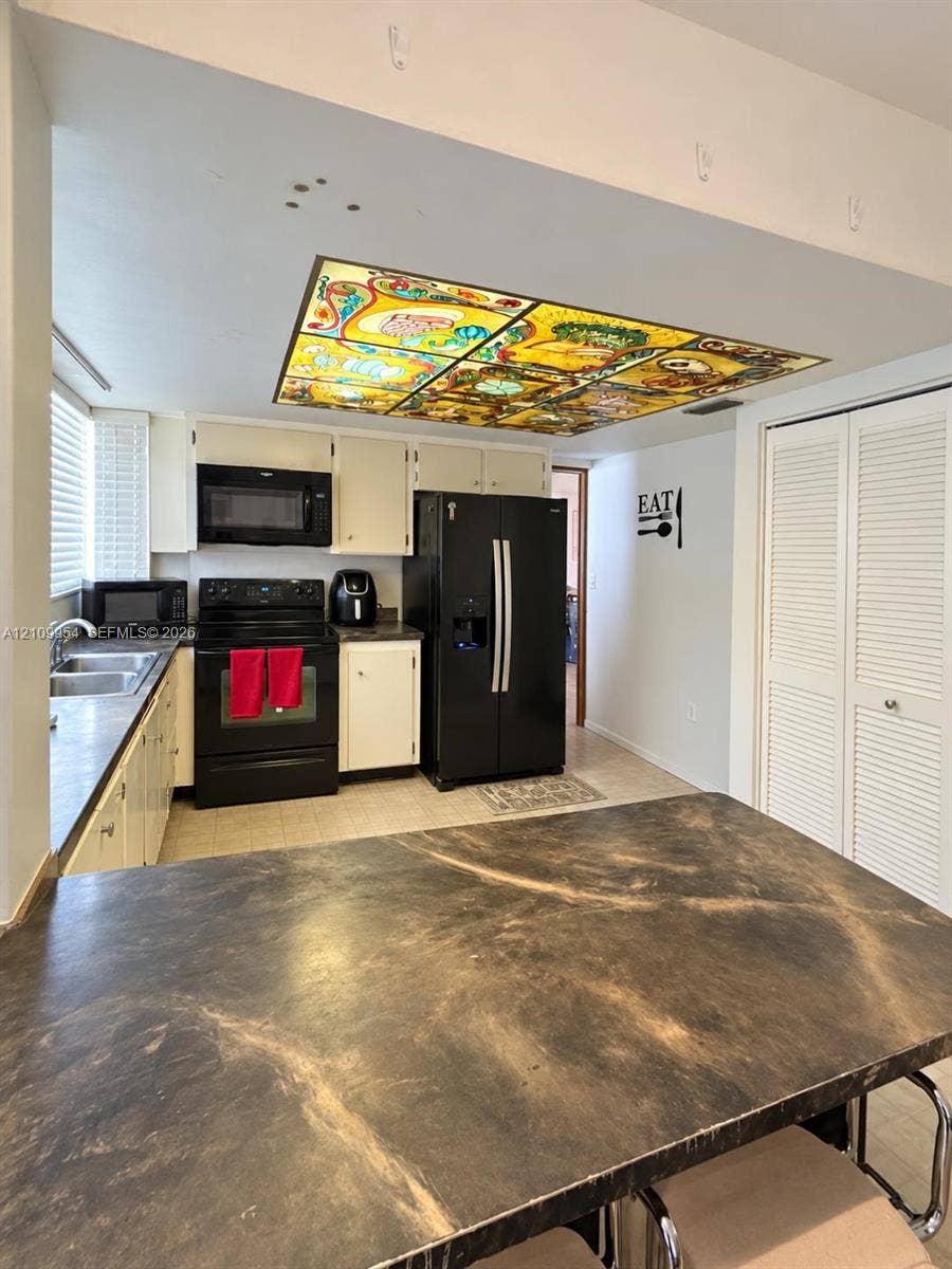 8528 Windsor Drive, Miramar, FL 33025 Kitchen featuring a decorative stained-glass ceiling fixture, dark-tone laminate countertops, solid-color cabinetry, black appliances, and louvered double-door storage