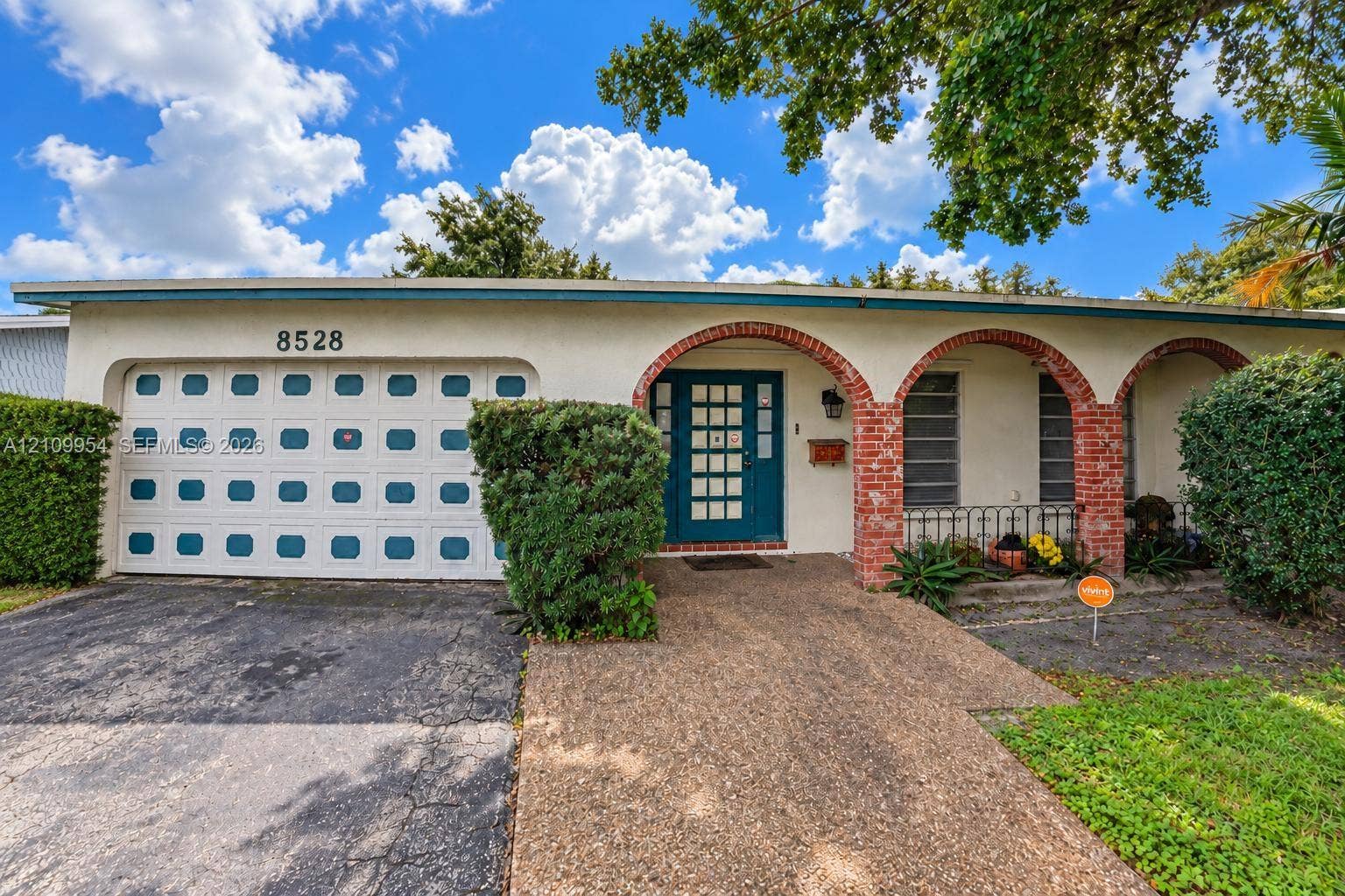 8528 Windsor Drive, Miramar, FL 33025 Single-story exterior featuring a stucco facade, red brick archway detail, aggregate concrete walkway, multi-pane front door, and a multi-panel garage door