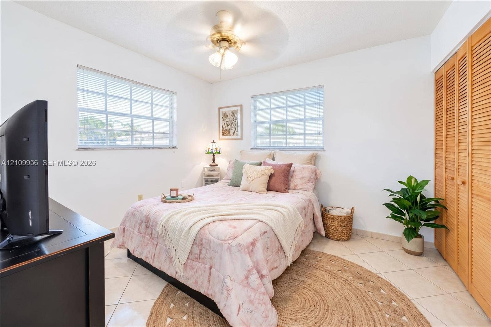 19503 SW 114th Place, Miami, FL 33157 Interior space featuring light-toned tile flooring, dual windows with grid-pattern glass, a ceiling fan with integrated lighting, and full-height bi-fold louvered closet doors