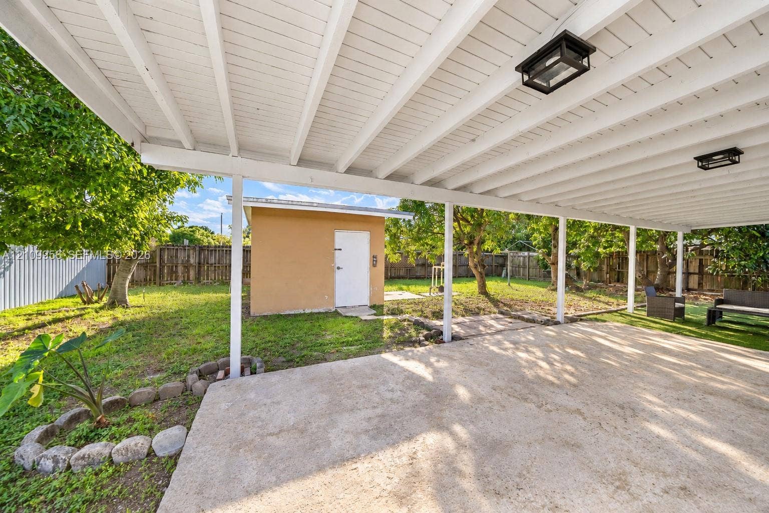 19503 SW 114th Place, Miami, FL 33157 Covered concrete patio with overhead lighting, detached storage building, and fenced backyard with mature trees