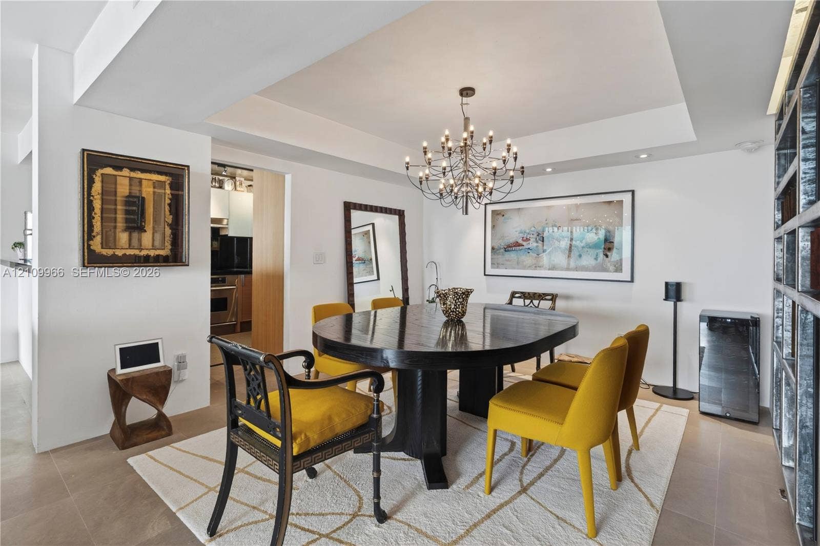 Dining area featuring a recessed tray ceiling, multi-arm chandelier, large-format tile flooring, and floor-to-ceiling built-in shelving
