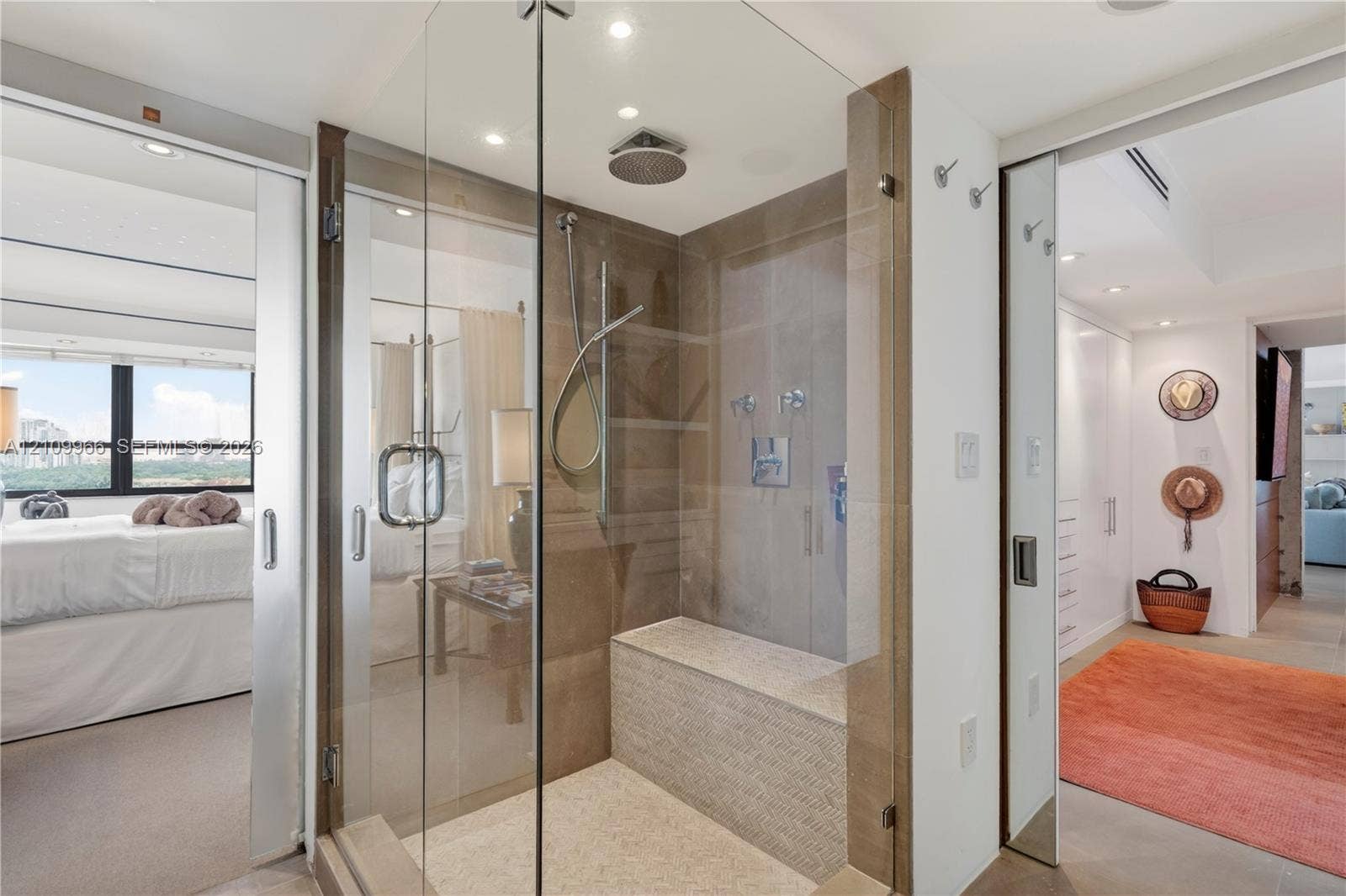 Walk-in glass-enclosed shower featuring a built-in stone bench, overhead rainfall showerhead, handheld sprayer, and neutral tile wall cladding