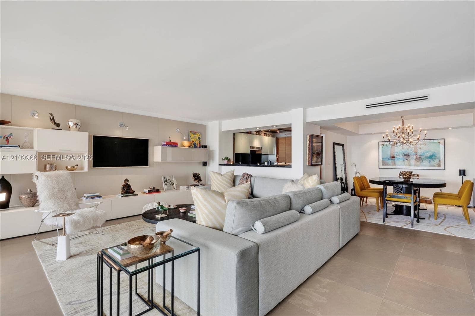 Open-concept interior featuring large-format tile flooring, built-in high-gloss cabinetry, recessed accent lighting, and a multi-tiered crystal chandelier