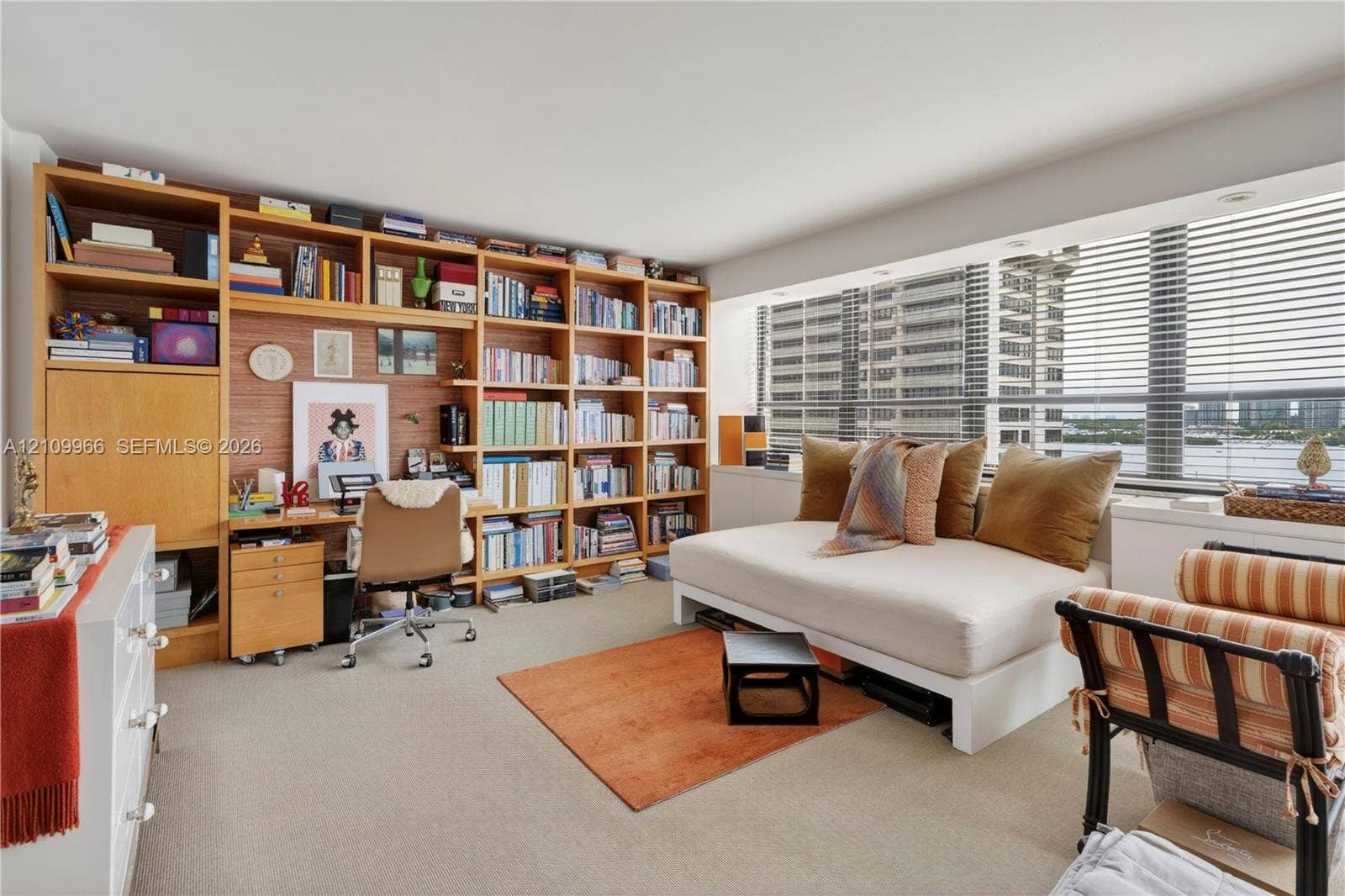 Built-in wall-to-wall wood shelving unit with integrated desk workspace and large windows featuring horizontal blinds