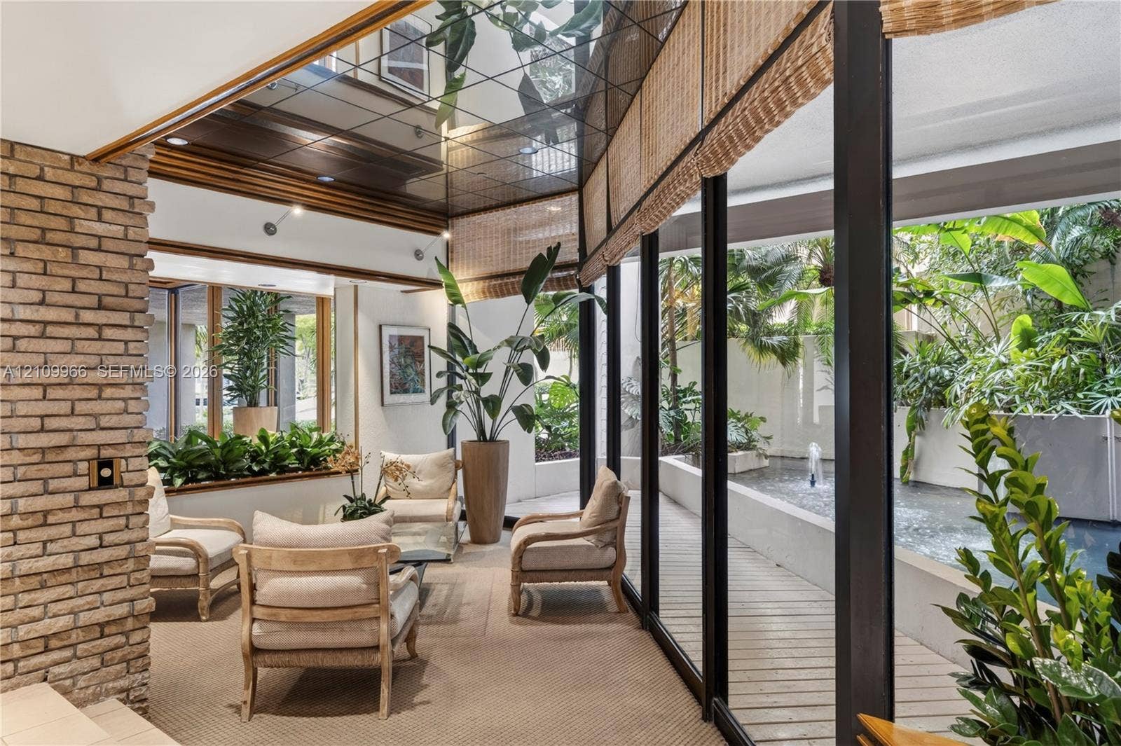 Interior space featuring a mirrored ceiling, exposed brick wall, floor-to-ceiling glass wall panels, and an outdoor water feature