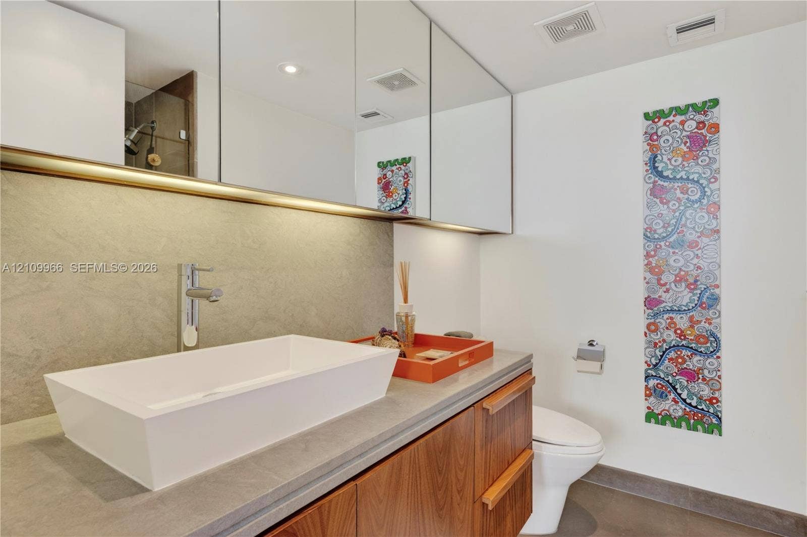 Wall-mounted wood-finish vanity with a rectangular vessel sink, solid-surface countertop, full-width mirrored cabinetry, and wall-mounted faucet
