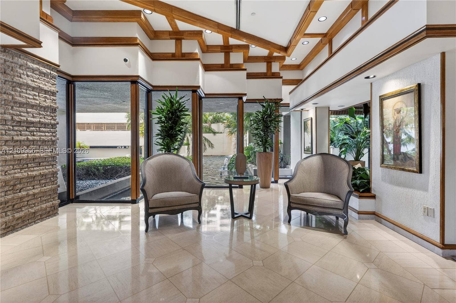 Vaulted ceiling with exposed wood-beam detailing, polished stone tile flooring, expansive floor-to-ceiling windows, and integrated stone masonry accent wall