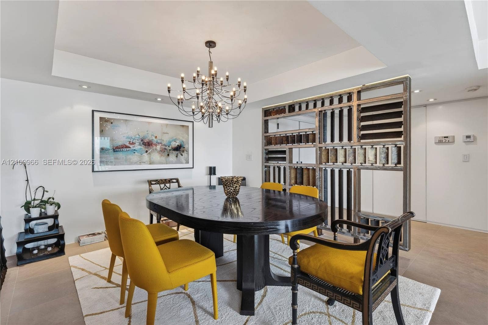 Tray ceiling with recessed lighting, multi-arm metal chandelier, and a custom decorative open-frame metal partition