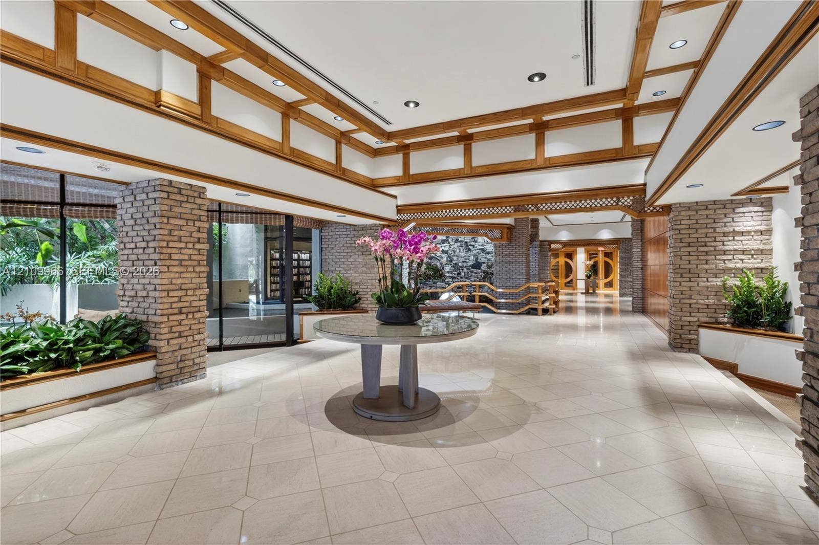 Spacious interior featuring a coffered ceiling with wood trim, decorative brick pillars, tile flooring, and recessed lighting