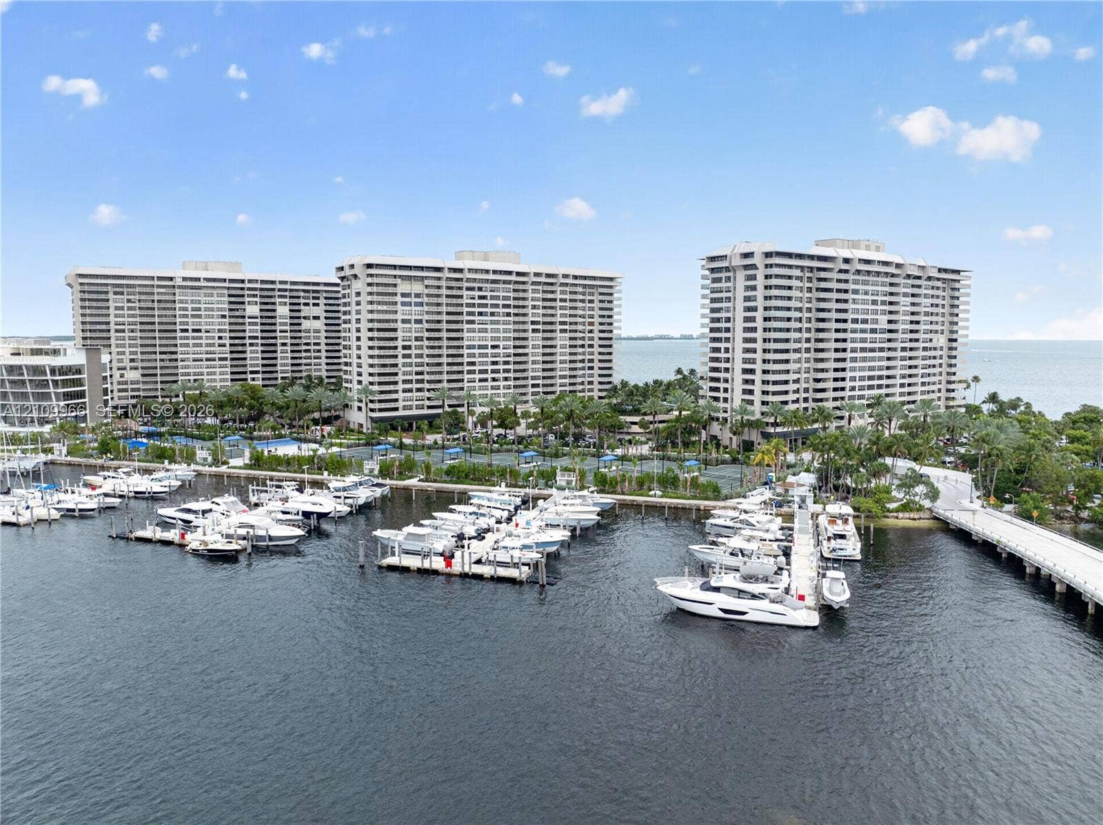 High-rise residential complex featuring a deep-water marina, private boat slips, extensive waterfront hardscaping, and lush tropical landscaping