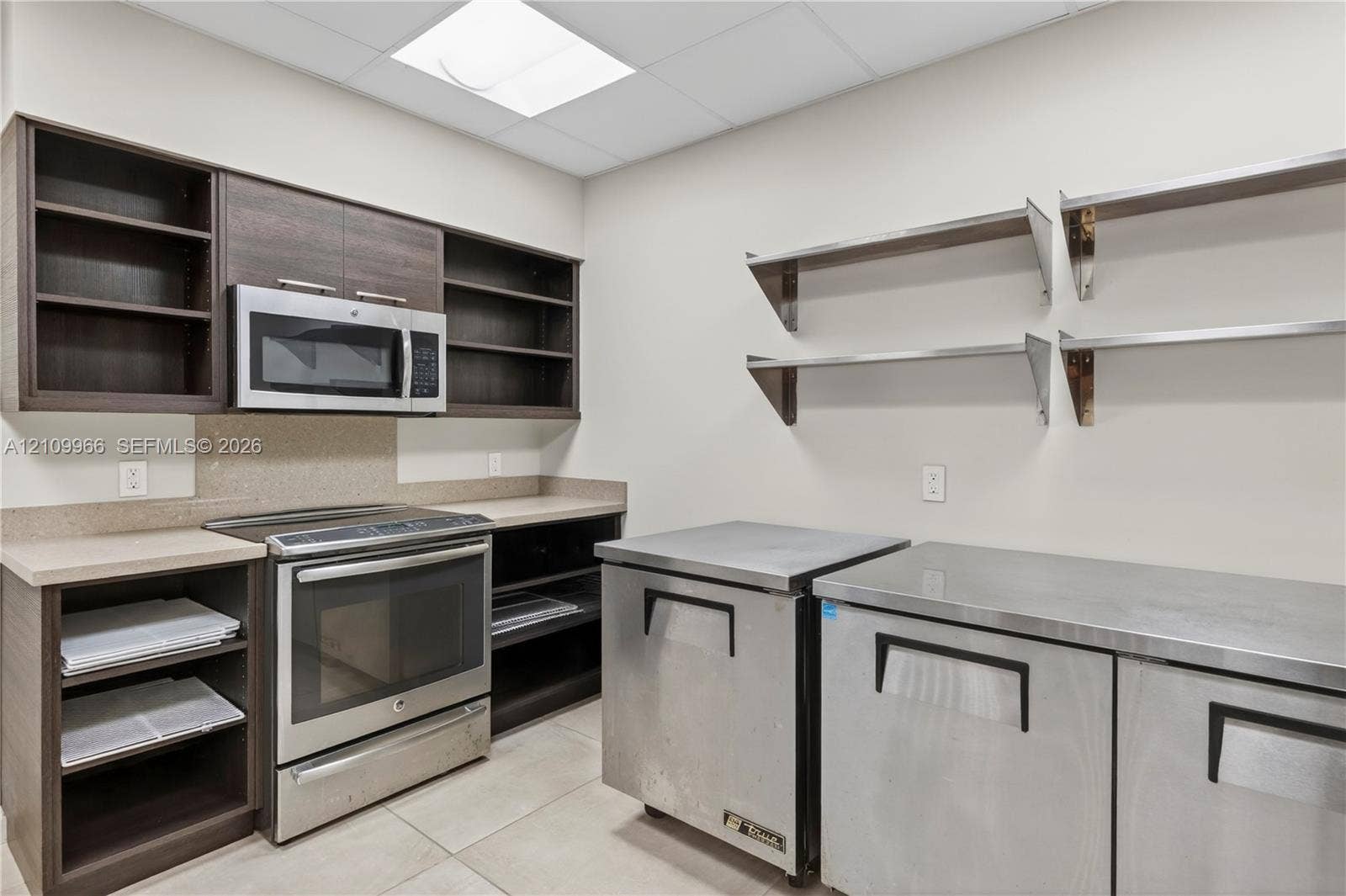 Kitchen area featuring dark wood-finish cabinetry, stainless steel appliances, open shelving, stone-composite countertops, and tile flooring