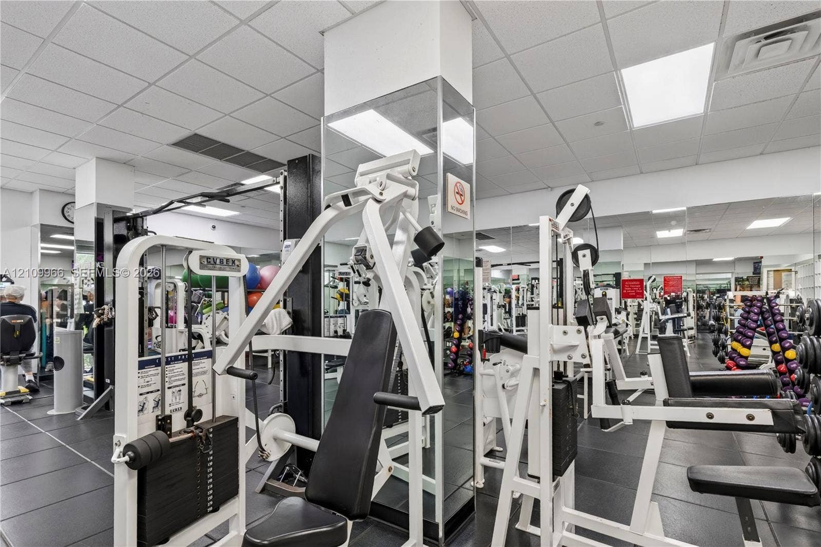 Fitness center featuring grid ceiling tiles, wall-to-wall mirrors, and durable rubber flooring