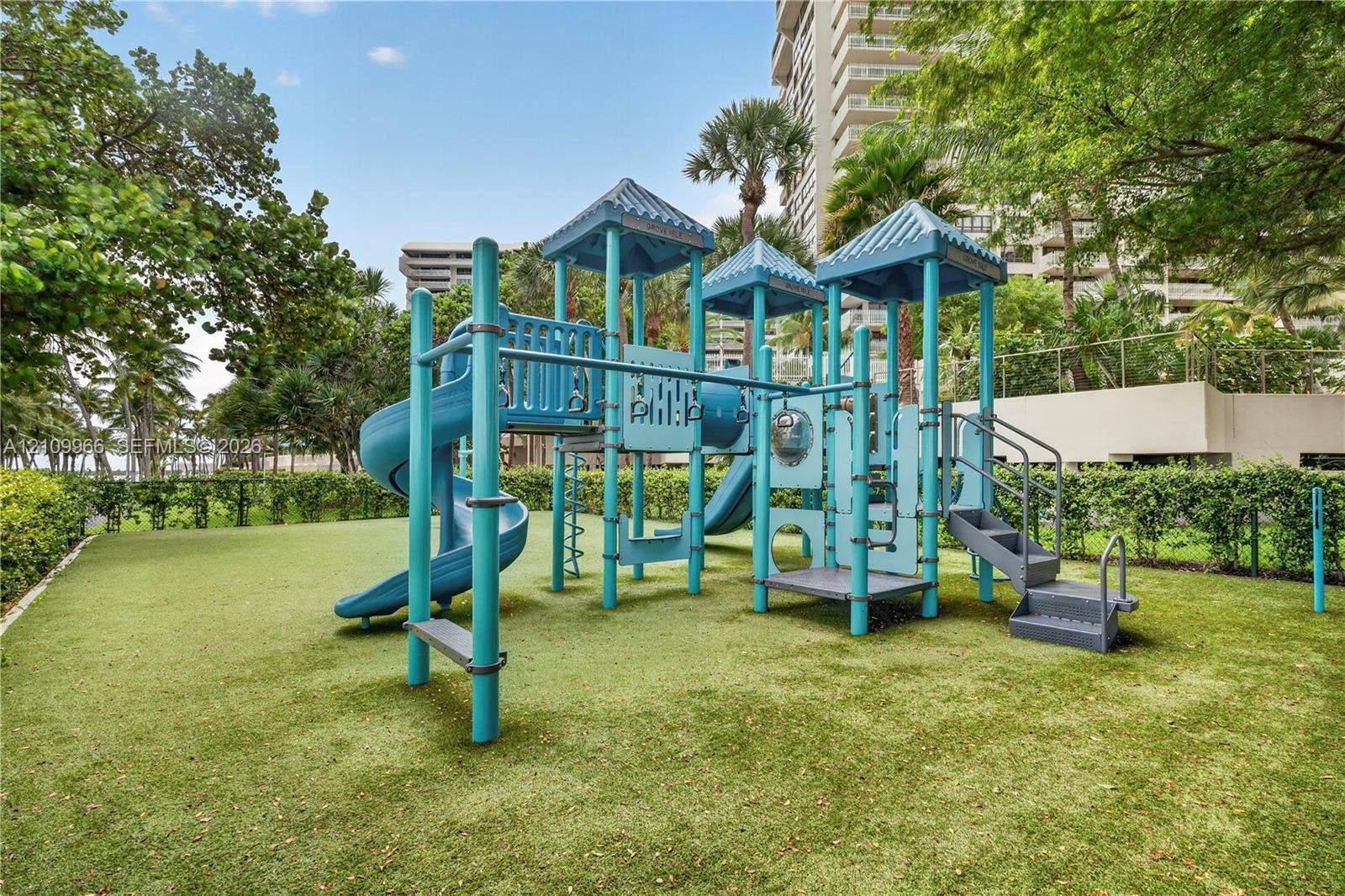 Recreational area featuring a multi-level climbing structure with integrated slides, stairs, and platforms situated on a manicured lawn enclosed by mature perimeter landscaping
