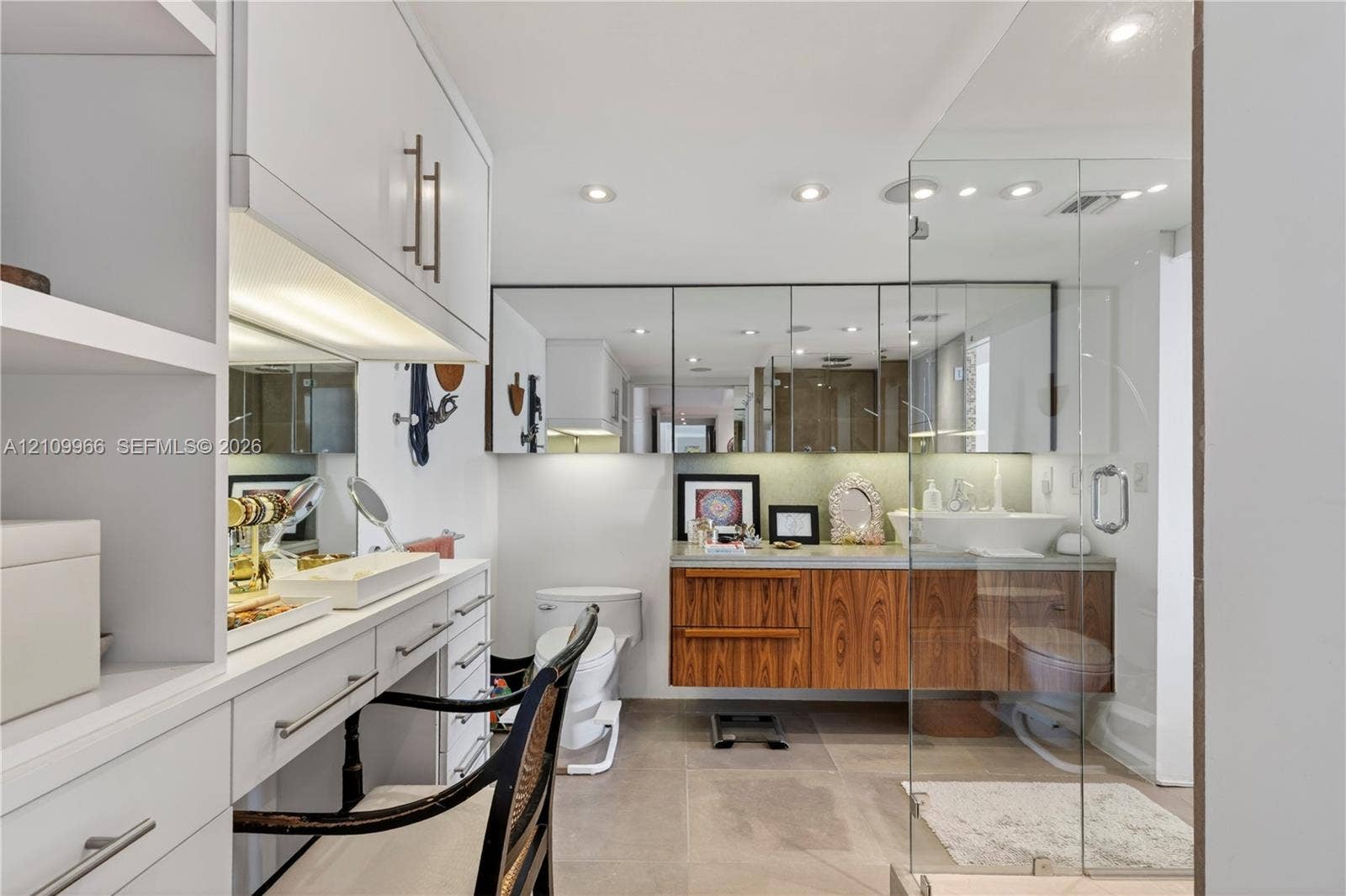 Wall-mounted wood-finish vanity with a rectangular vessel sink, integrated medicine cabinet mirrors, recessed lighting, and a glass-enclosed shower featuring large-format tile flooring
