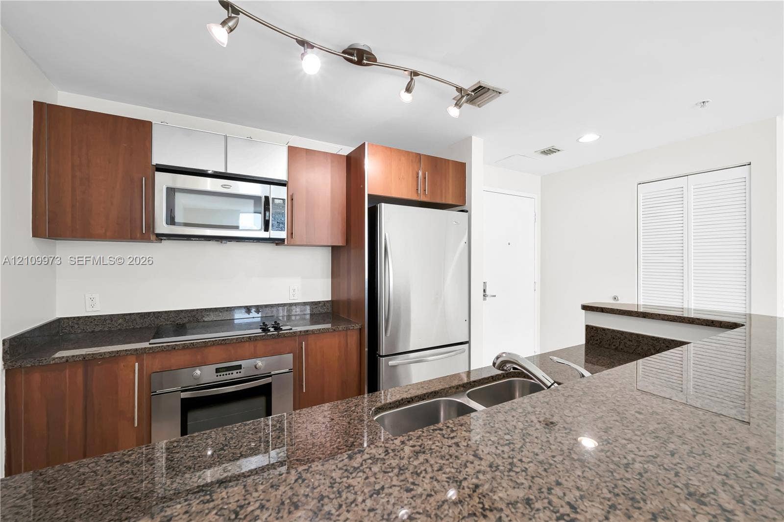 300 S Biscayne Boulevard, #T-1806, Miami, Miami, FL 33131 Kitchen featuring wood-finish cabinetry, stone countertops, stainless steel appliances, double-basin sink, and track lighting