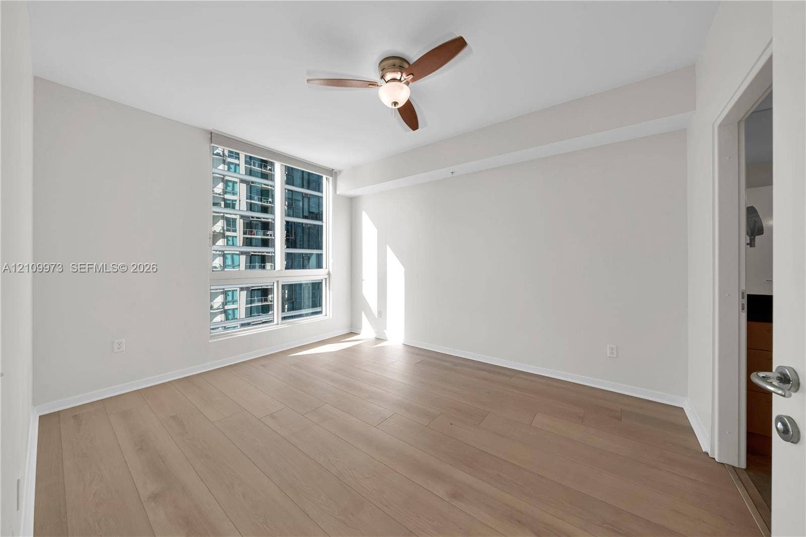 300 S Biscayne Boulevard, #T-1806, Miami, Miami, FL 33131 Neutral-toned interior featuring wide-plank wood-finish flooring, floor-to-ceiling windows, and a three-blade ceiling fan with an integrated light fixture