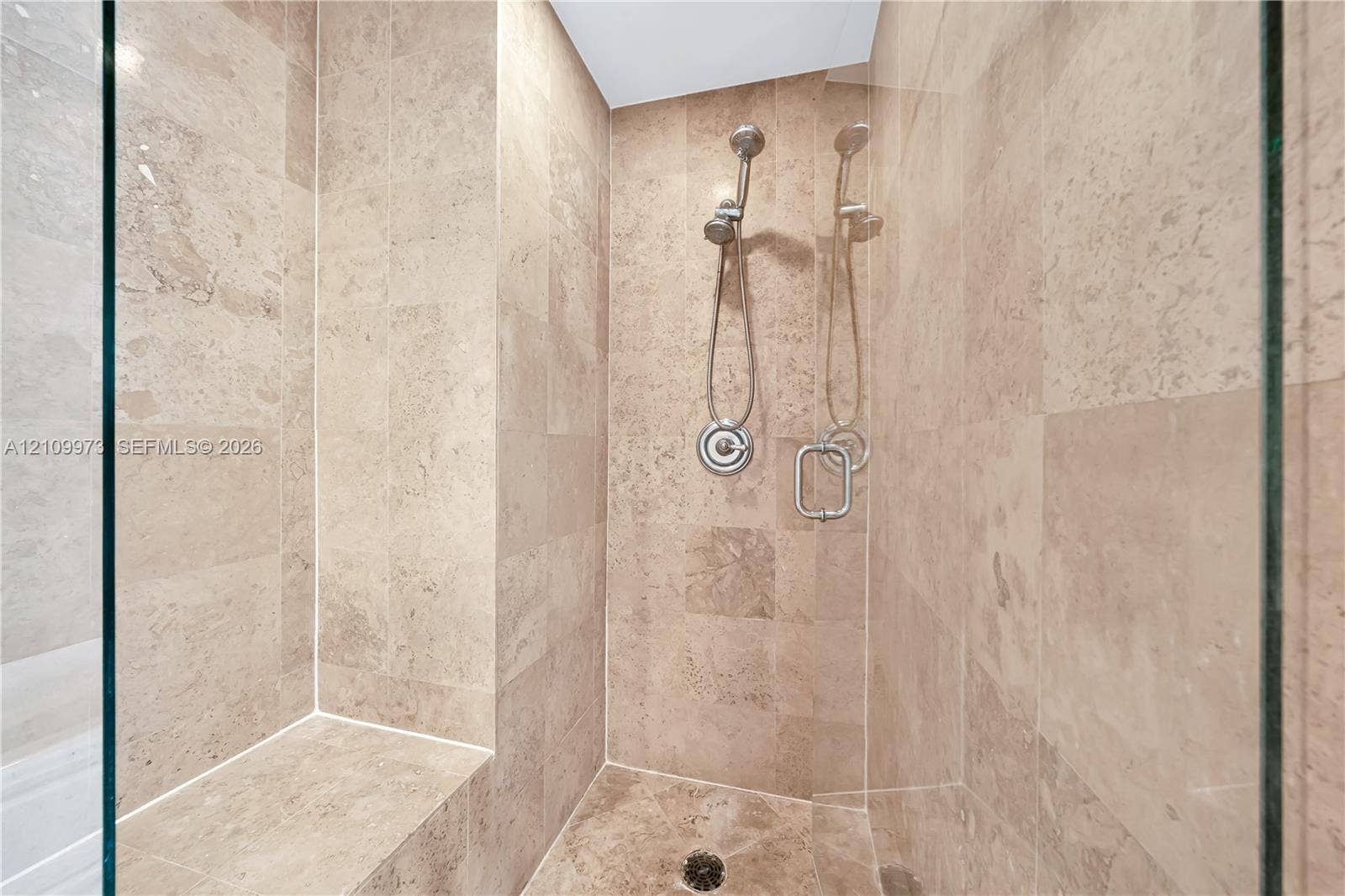 300 S Biscayne Boulevard, #T-1806, Miami, Miami, FL 33131 Walk-in shower featuring floor-to-ceiling stone tile, built-in stone bench, glass enclosure, and adjustable handheld shower fixture