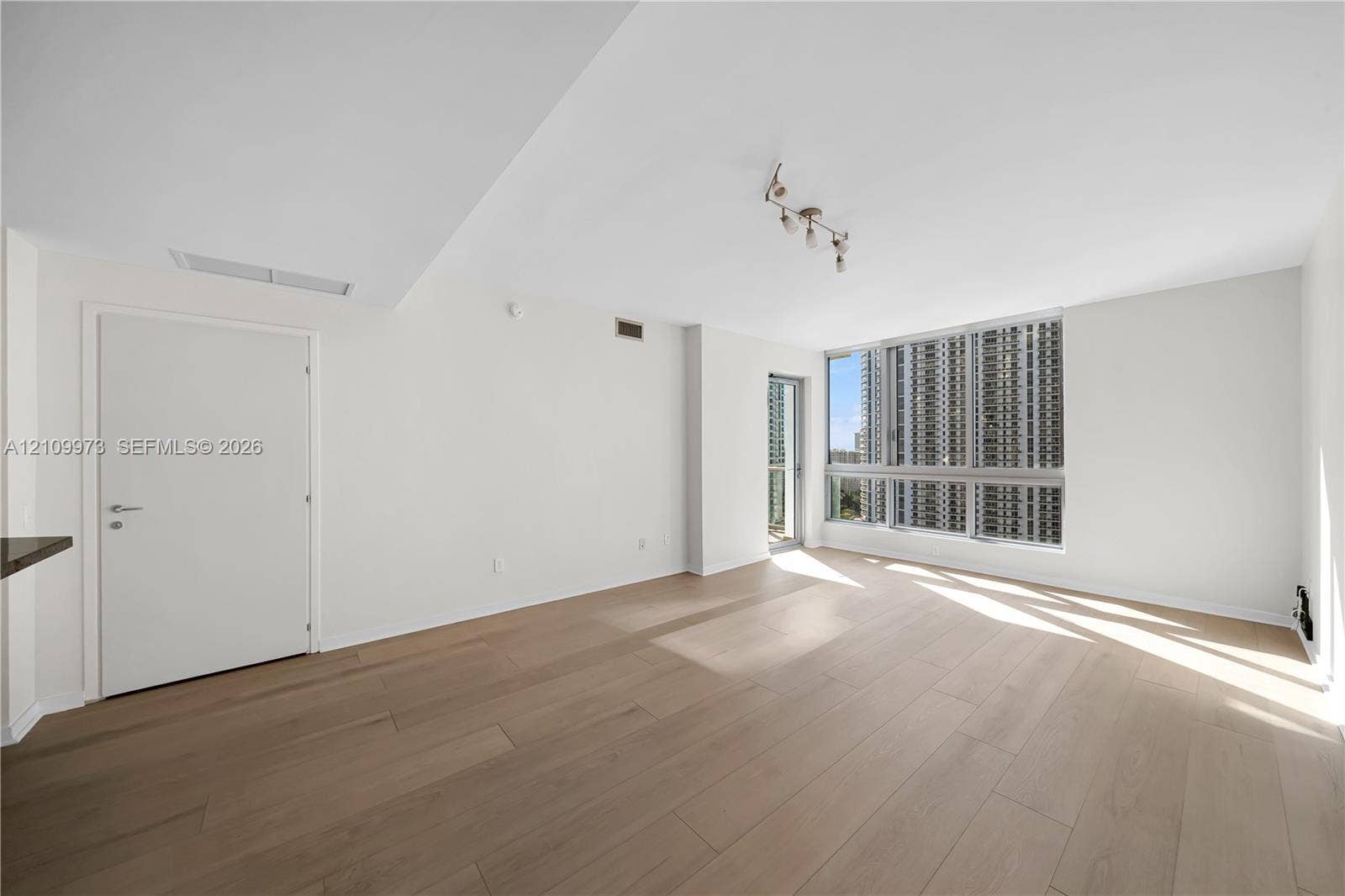 300 S Biscayne Boulevard, #T-1806, Miami, Miami, FL 33131 Interior space featuring wood-finish flooring, floor-to-ceiling windows, modern multi-bulb track lighting, and a glass-panel door leading to a balcony