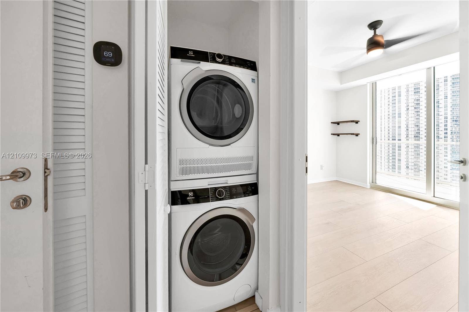 300 S Biscayne Boulevard, #T-1806, Miami, Miami, FL 33131 Stackable laundry unit featuring an Electrolux washer and dryer, digital wall-mounted thermostat, wood-finish flooring, ceiling fan with integrated lighting, and wall-mounted shelving