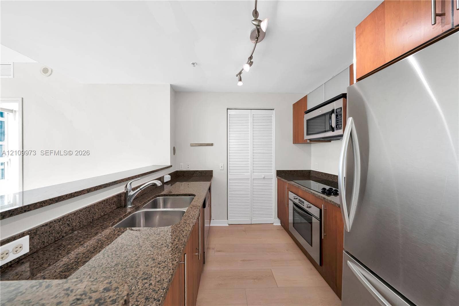 300 S Biscayne Boulevard, #T-1806, Miami, Miami, FL 33131 Kitchen featuring wood-finish cabinetry, stone countertops, stainless steel appliances, dual-basin sink, and track lighting