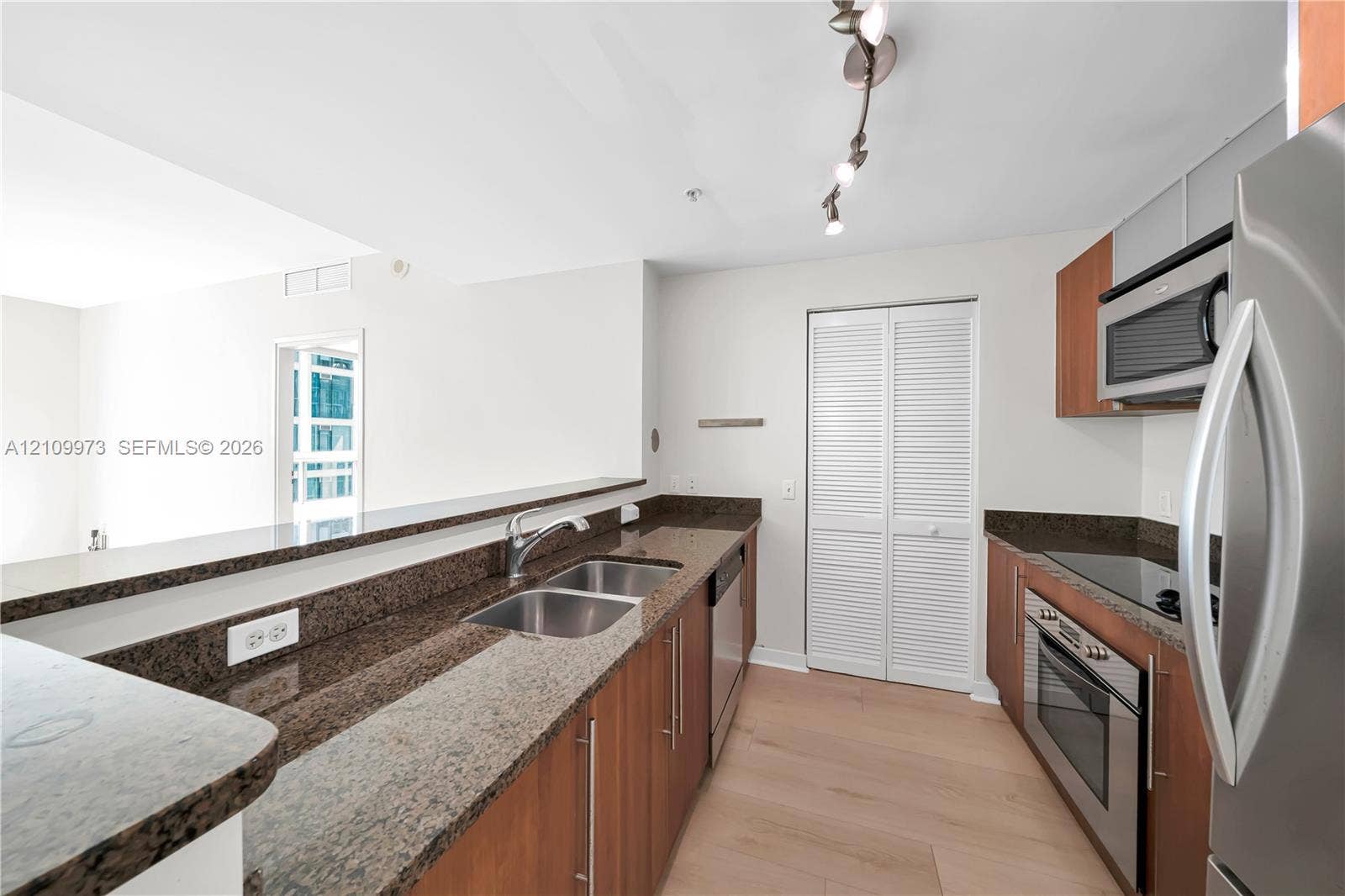 300 S Biscayne Boulevard, #T-1806, Miami, Miami, FL 33131 Kitchen featuring wood-finish cabinetry, stone countertops, stainless steel appliances, dual-basin sink, and track lighting